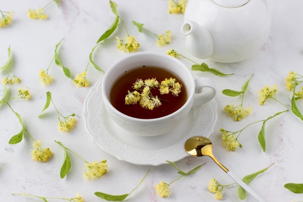 Tea with linden in a white cup on a white marble table White teapot with aromatic tea