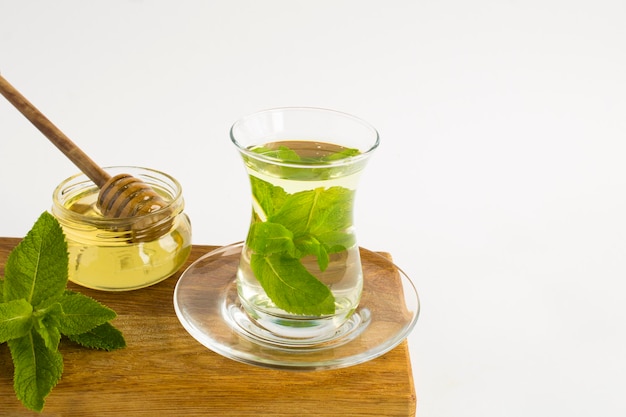 Tea with mint and honey in the glass cup on the white background Closeup Copy space