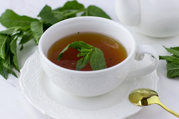 Tea with mint in a white cup and a white teapot on a white marble background Morning tea