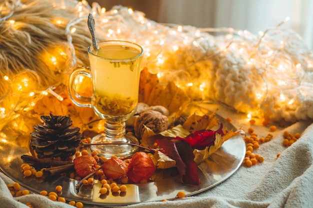 Tea with sea-buckthorn berries and ginger on old books, honey, candle and autumn leaves. The atmosphere of comfort at home. Warm cozy home.