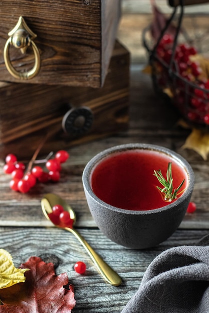 Tea with viburnum berries in a bowl decorated rosemary on a wooden table