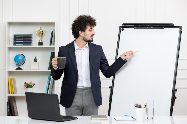 Teacher brunette instructor with computer in suit and whiteboard in classroom pointing at board