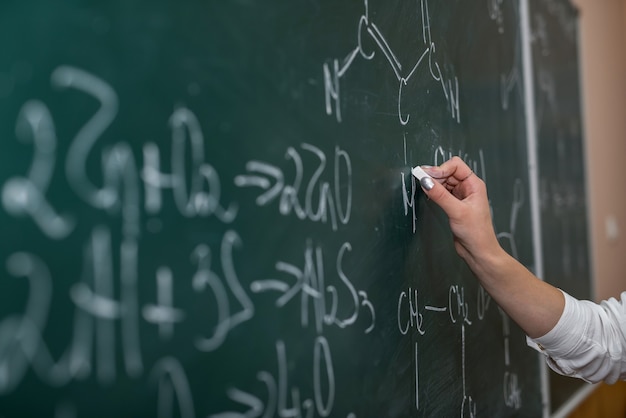 Teacher hand holding pointer and showing formulas in chemistry lesson on blackboard. Offline education