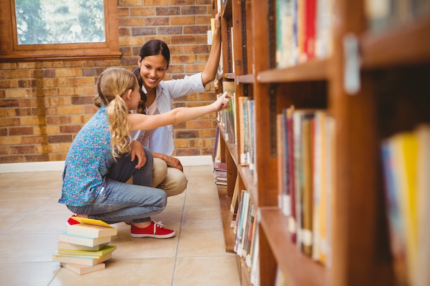 Teacher and little girl selecting book in library