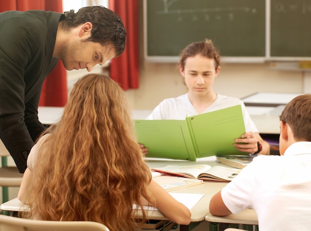 Teacher standing while math lesson in front of a blackboard and educates students in class