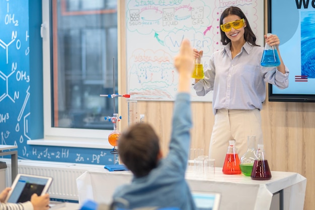 Teacher with flasks asking and student with raised hand