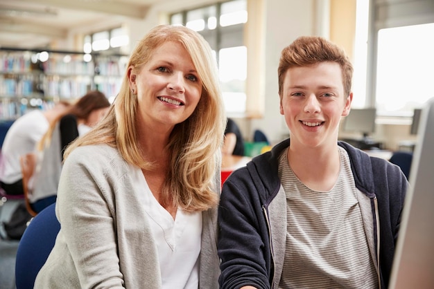 Teacher With Male Student Working On Computer In College Library