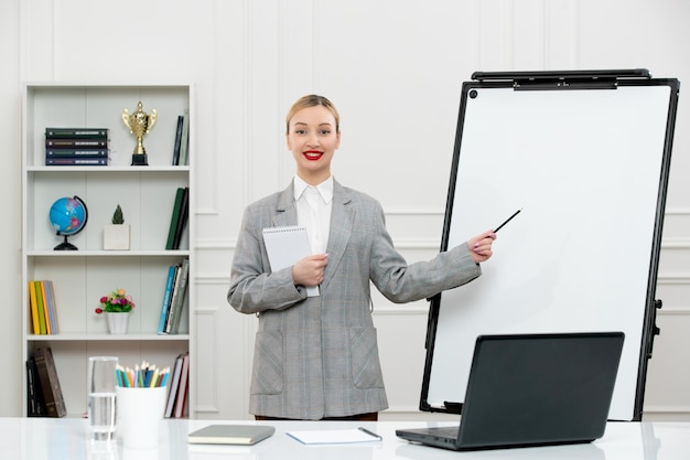 Teacher young cute instructor in suit in classrom with laptop and whiteboard pointing at board