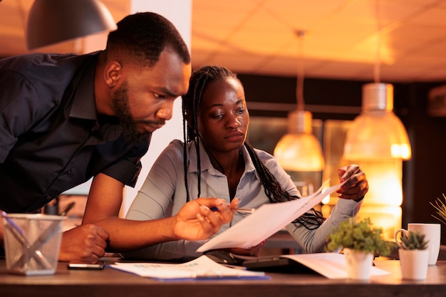 Team of african american business partners analyzing documents information with computer. Working on teamwork collaboration to create startup company report with research and data.