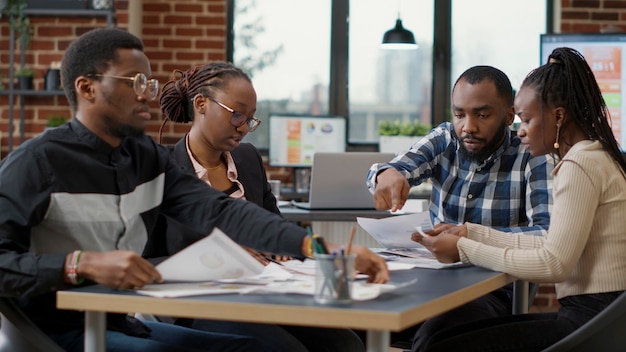 Team of african american businesspeople analyzing charts documents, looking at report statistics and financial research on papers. Work colleagues collaborating on presentation. Tripod shot.