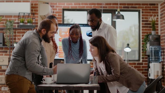 Team of colleagues brainstorming ideas to plan project and business strategy together in startup office. People working on marketing strategy design and presentation, looking at laptop.