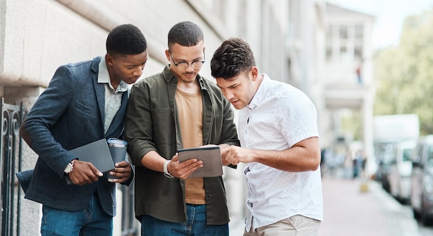 Team of creative designers checking a website for ux and ui while working for a startup Group of young guys looking at a homepage on a tablet while developing a new business strategy or mission