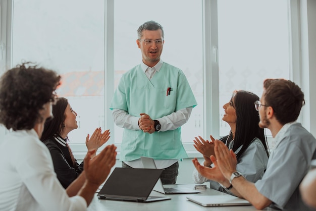 A team of doctors and a medical nurse applauding their colleague after a presentation in a meeting room