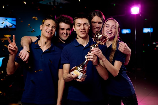 Team of excited teenage participants of e-sports video gaming competition showing prize for their victory