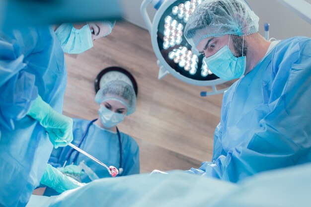 Team of experienced surgeons working together in the operating theatre. Concentrated faces of three doctors