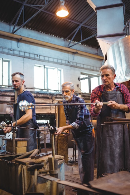 Team of glassblowers shaping a glass on the blowpipe