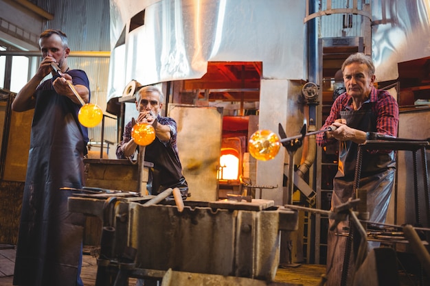 Team of glassblowers shaping a glass on the blowpipe