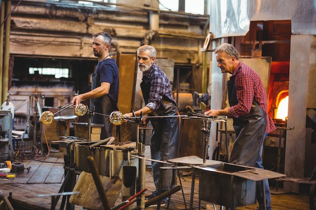 Team of glassblowers shaping a glass on the blowpipe