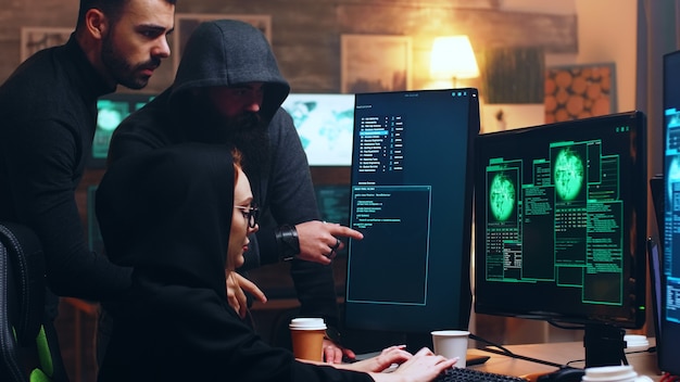 Team of hackers looking at computer with multiple monitors while committing cyber crimes.