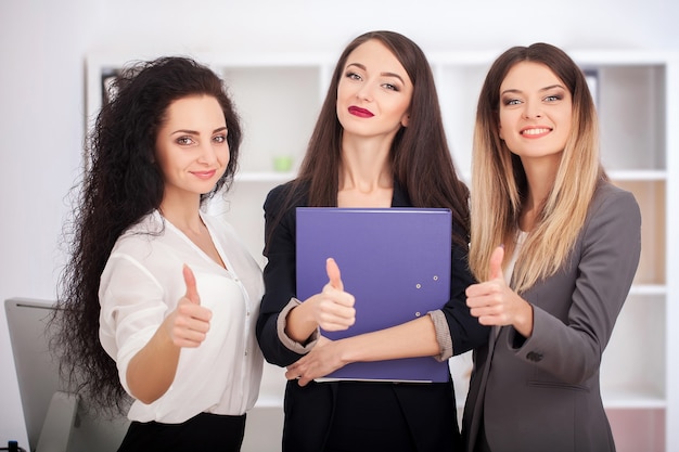 Team portrait of happy businesswomen standing on office corridor, looking at camera, smiling.