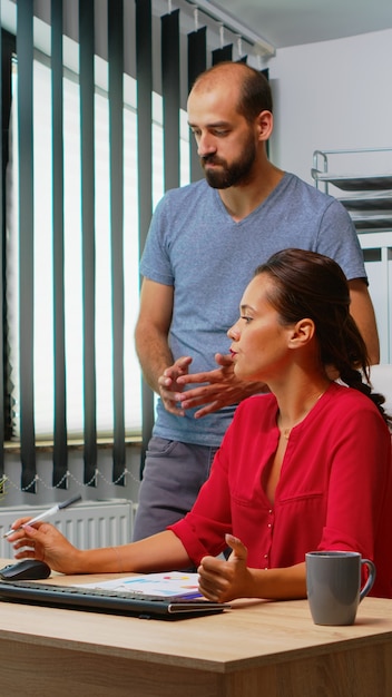 Team searching the best solution in front of computer in modern office room. Coworkers discussing working in workplace in personal corporate company typing on pc keyboard pointing at desktop