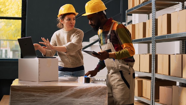 Team of workers analyzing logistics for merchandise production in warehouse space, checking barcodes before planning shipment. Man and woman discussing about inventory service.