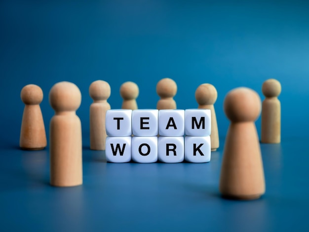 Teamwork team leadership and family business concepts Words TEAMWORK text on white cube blocks and different wooden people figures standing in front of the big target icon on blue background