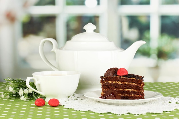 Teapot cup of tea and delicious cake on window background