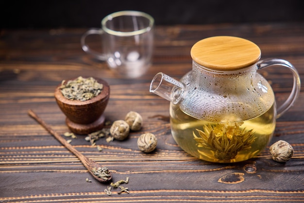 Teapot and glass cup with blooming tea flower inside on a wooden table