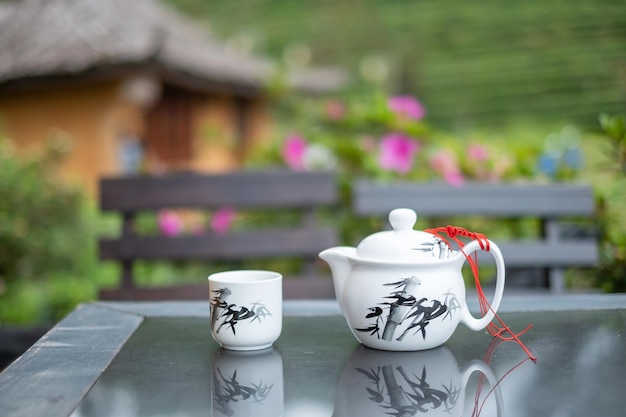 Teapot and hot tea to cup on wood table against tea garden view background in the morning Ban Rak Thai village Mae Hong Son province Thailand