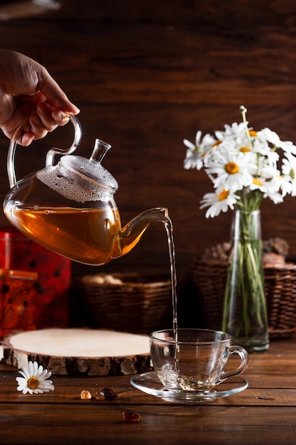 A teapot and a mug of tea on a wooden table and a bouquet of daisies