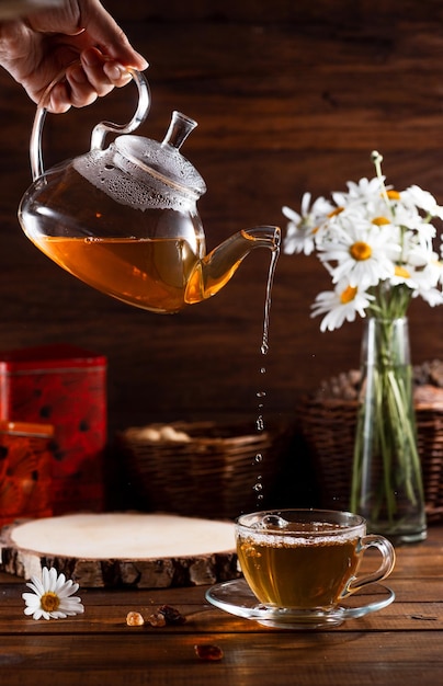 A teapot and a mug of tea on a wooden table and a bouquet of daisies