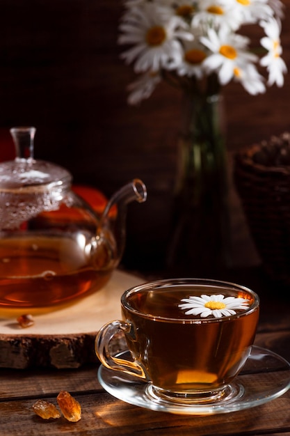 A teapot and a mug of tea on a wooden table and a bouquet of daisies