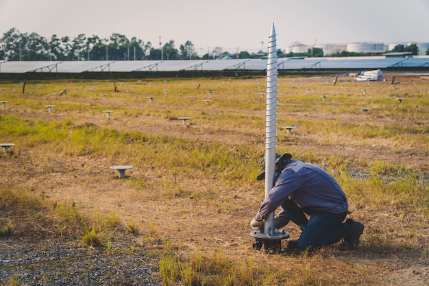 Technician installing ground screw for mounting structure of solar panel at solar farm