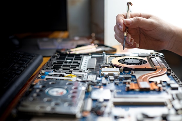 Technician repairing broken laptop notebook computer with screwdriver