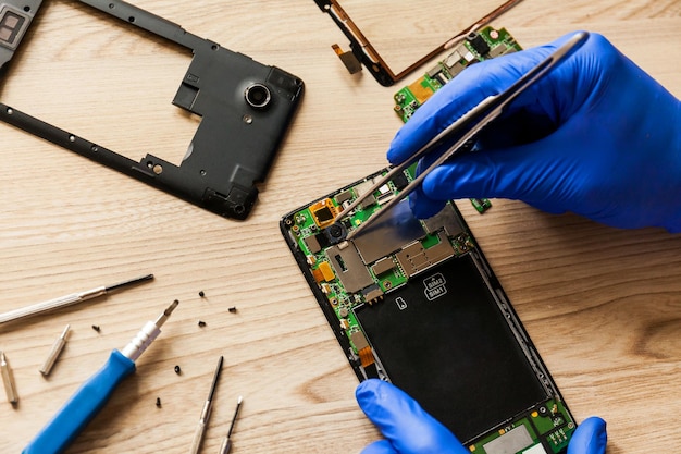 The technician repairing the smartphone's motherboard in the workshop on the table