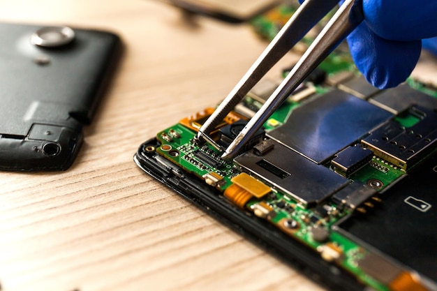 The technician repairing the smartphone's motherboard in the workshop on the table