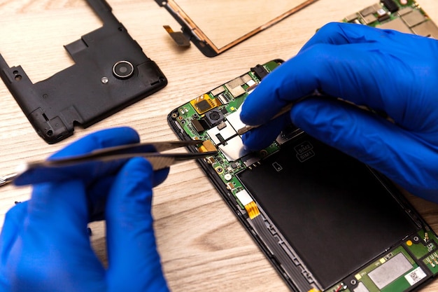 The technician repairing the smartphone's motherboard in the workshop on the table