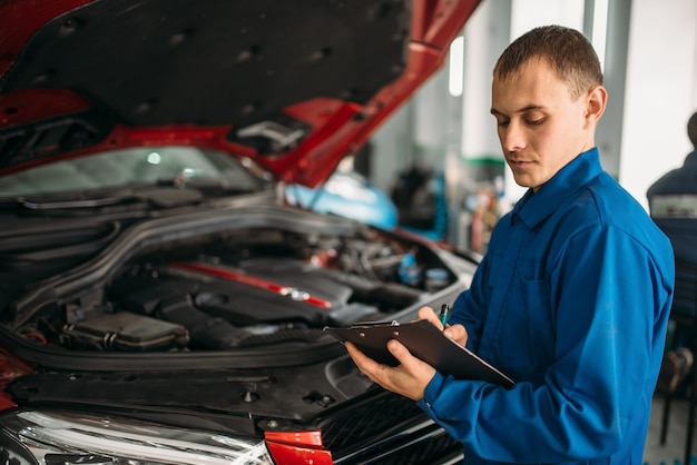 Technician with notebook, car with opened hood