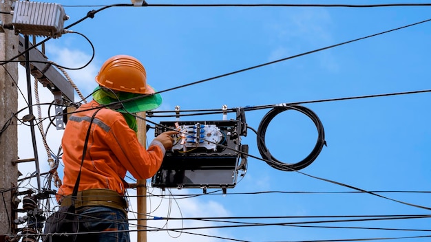 Technician on wooden ladder checking fiber optic cables in internet splitter box on electric pole