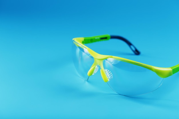 Technological protective green glasses isolated on a blue background. Reliable eye protection, free space