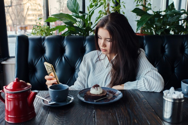 Technologies emotions lifestyle people teens concept Young happy female reading on her mobile phone while sitting in modern coffee shop interior girl with beautiful smile drink tea