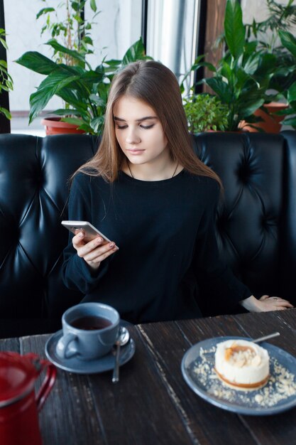 Technologies, emotions, lifestyle, people, teens concept -Young happy female reading on her mobile phone while sitting in modern coffee shop interior, gorgeous hipster girl with beautiful smile