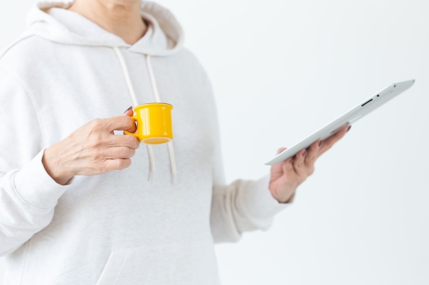 Technologies and modern people concept - Close-up of woman holding tablet and small yellow cup of coffee in light room