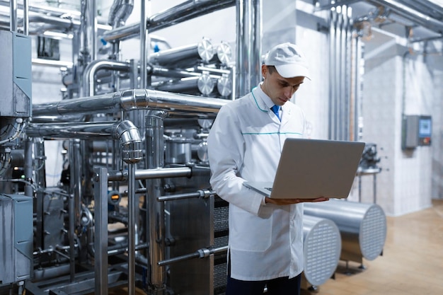 Technologist in a white coat with a laptop in his hands controls the production process in the dairy shop Quality control at the dairy plant