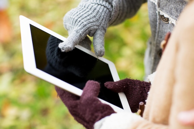 technology, advertisement and people concept - close up of couple hands in autumn gloves holding tablet pc computer outdoors