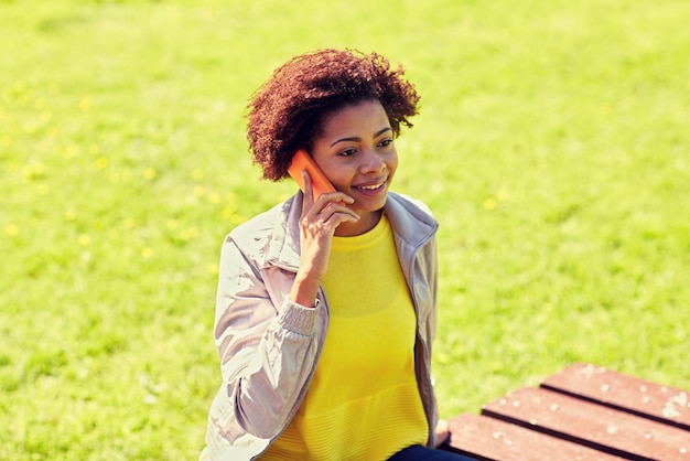 technology, communication and people concept - smiling african american young woman or teenage girl calling on smartphone outdoors