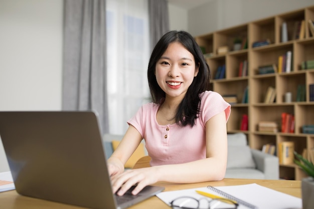 Technology concept Excited asian lady sitting at desk and looking at camera using laptop in living room