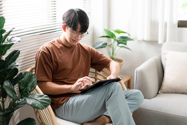 Technology Concept The male with his casual T-shirt and jeans sitting comfortably on the wooden chair and doing touchscreen for checking the web browser on the iPad.