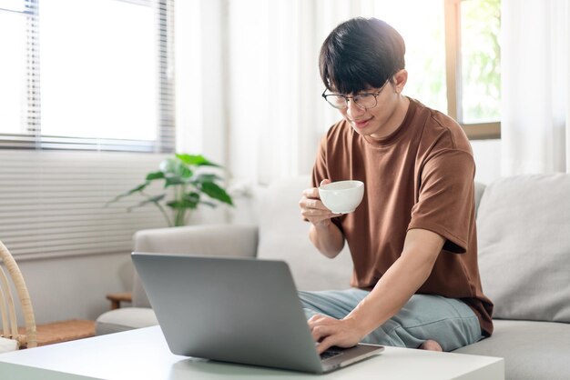 Technology Concept The man in brown T-shirt using one hand typing on his laptop while another hand holding a cup of coffee.